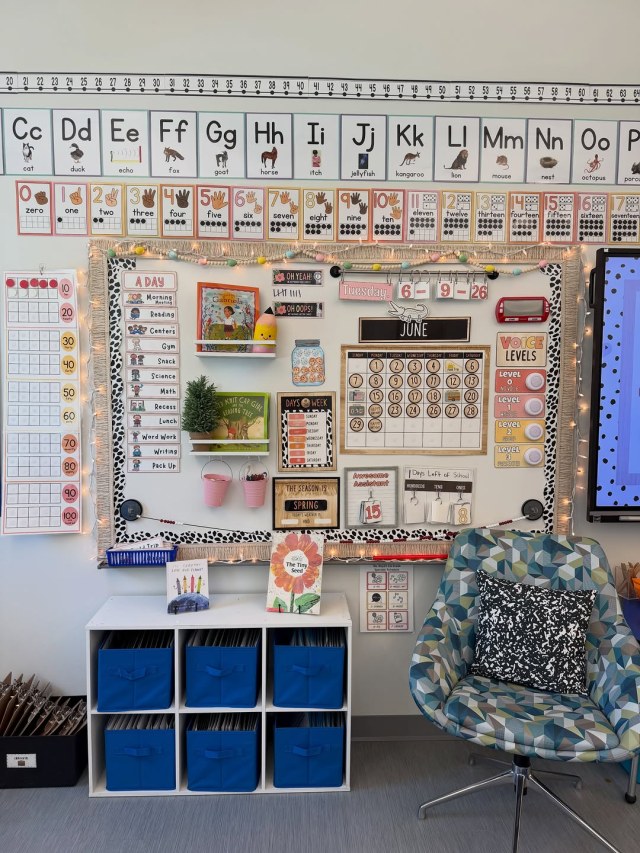 Classroom focus wall with alphabet cards, number posters, fringed calendar board, cubby with blue bins and swivel chair
